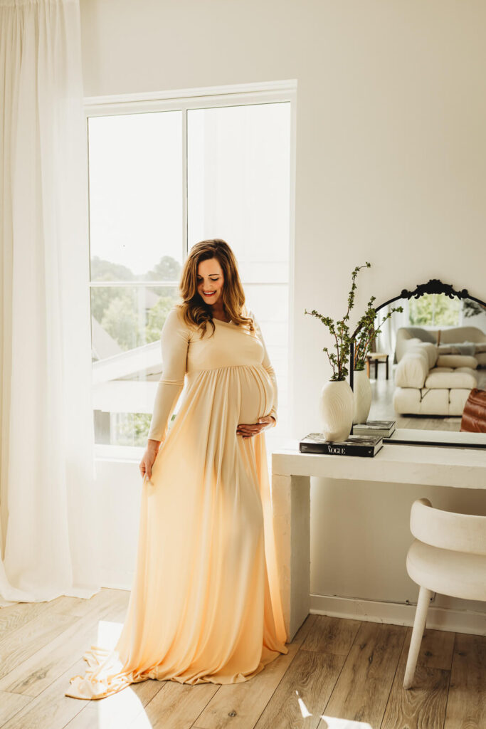 Mother-to-be standing in soft window light in a minimal studio setting