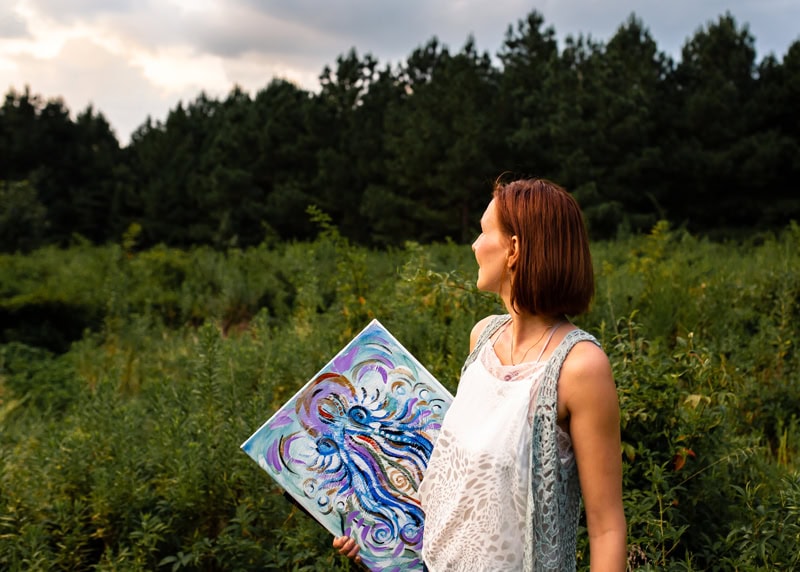 Artist holding colorful abstract artwork outdoors.