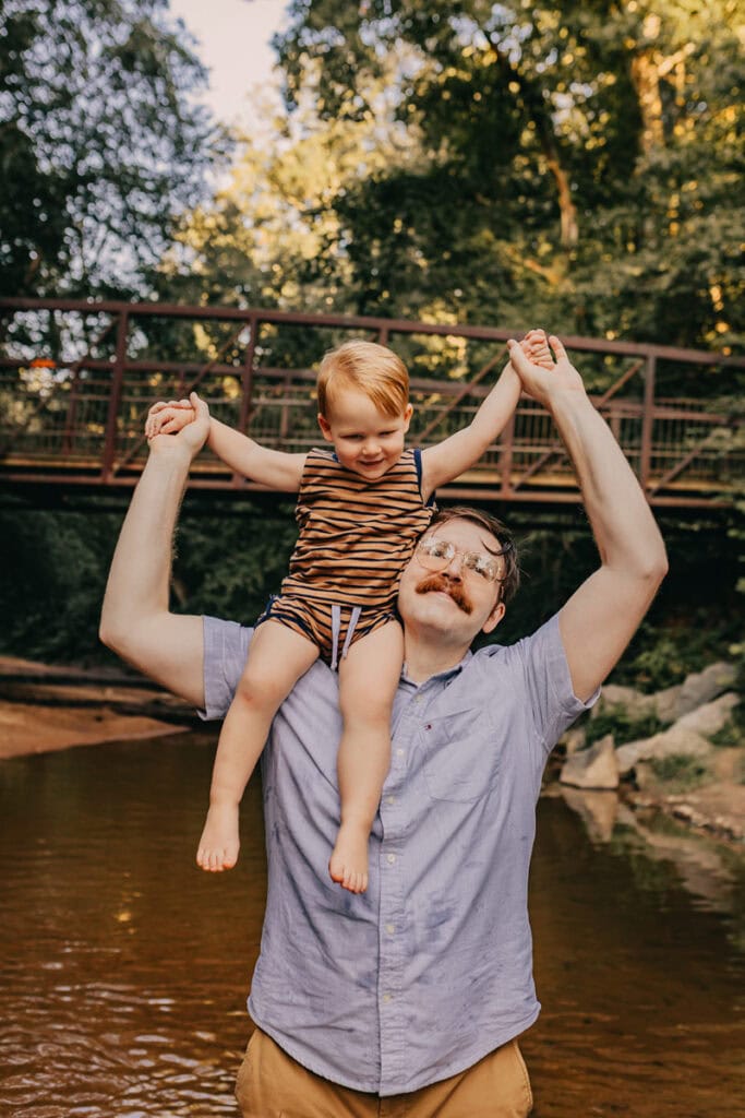 Father and young child enjoying a playful moment by the river in a park.